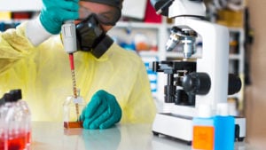 a scientist with protective equipment and microscope in a lab, OBSV stock. penny stocks to buy