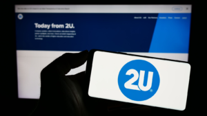 Person holding smartphone with logo of American educational technology company 2U Inc. on screen in front of web page. Focus on phone display. Unmodified photo. TWOU stock